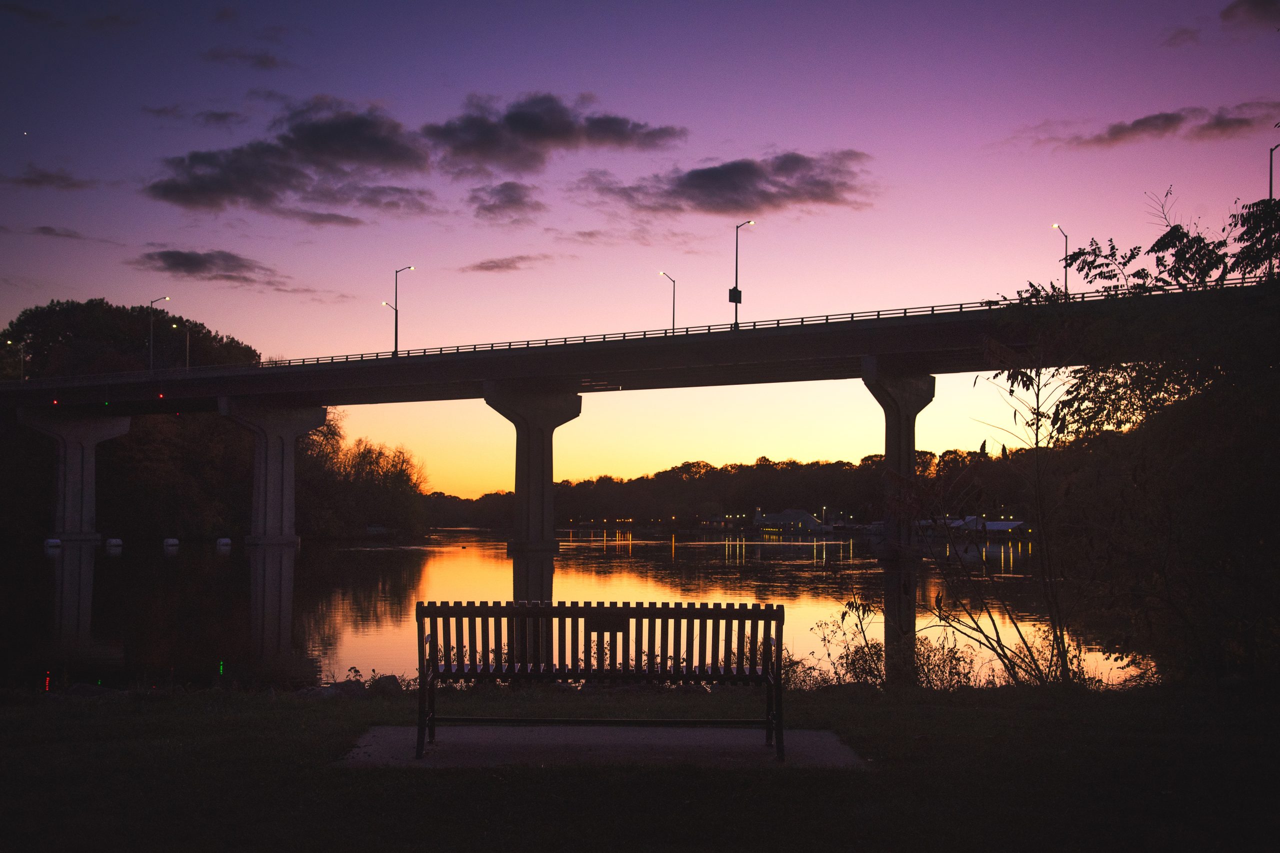 a bench sitting under a bridge next to a body of water